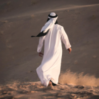 a man dresses like saudi arabians walks in the desert 
